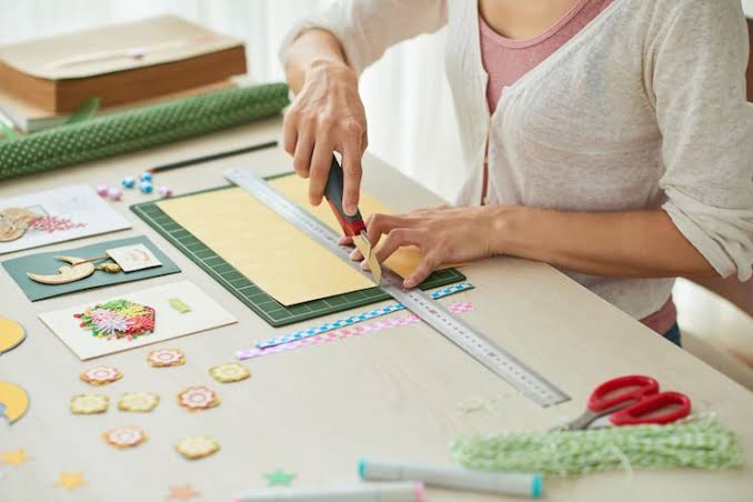 Hands measuring and cutting card stock with a ruler and craft knife