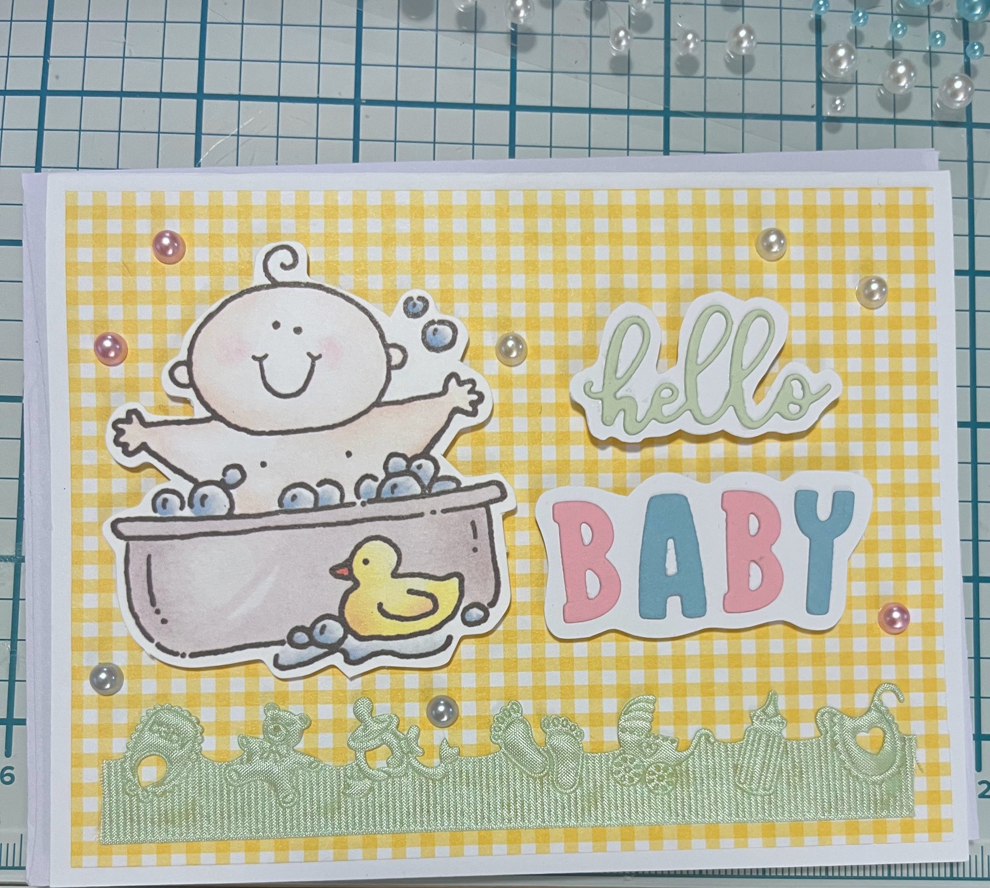 Handmade baby card on yellow gingham paper with a stamped baby in a bathtub, a rubber duck, pastel pearls, a green baby-toy ribbon border and die-cut &lsquo;hello BABY&rsquo; lettering